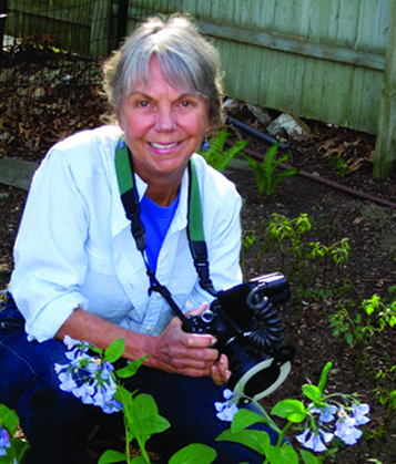 photo of smiling woman, Carol Gracie, in a garden holding a camera