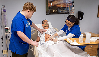 ni=ursing students in blue scrubs with dummy patient