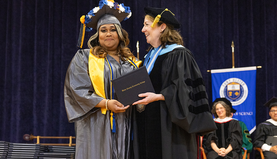 black woman with flowers on cap receiving diploma from Dean at SUNY Ulster graduation ceremony