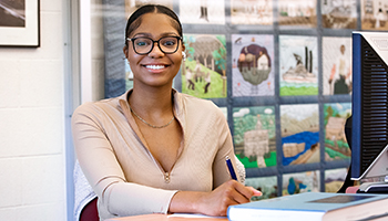 black female student in library writing in notebook