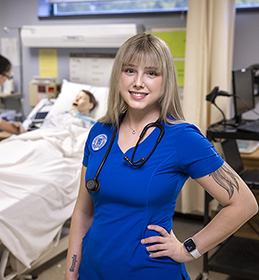 young woman in blue scrubs with dummy in hospital bed