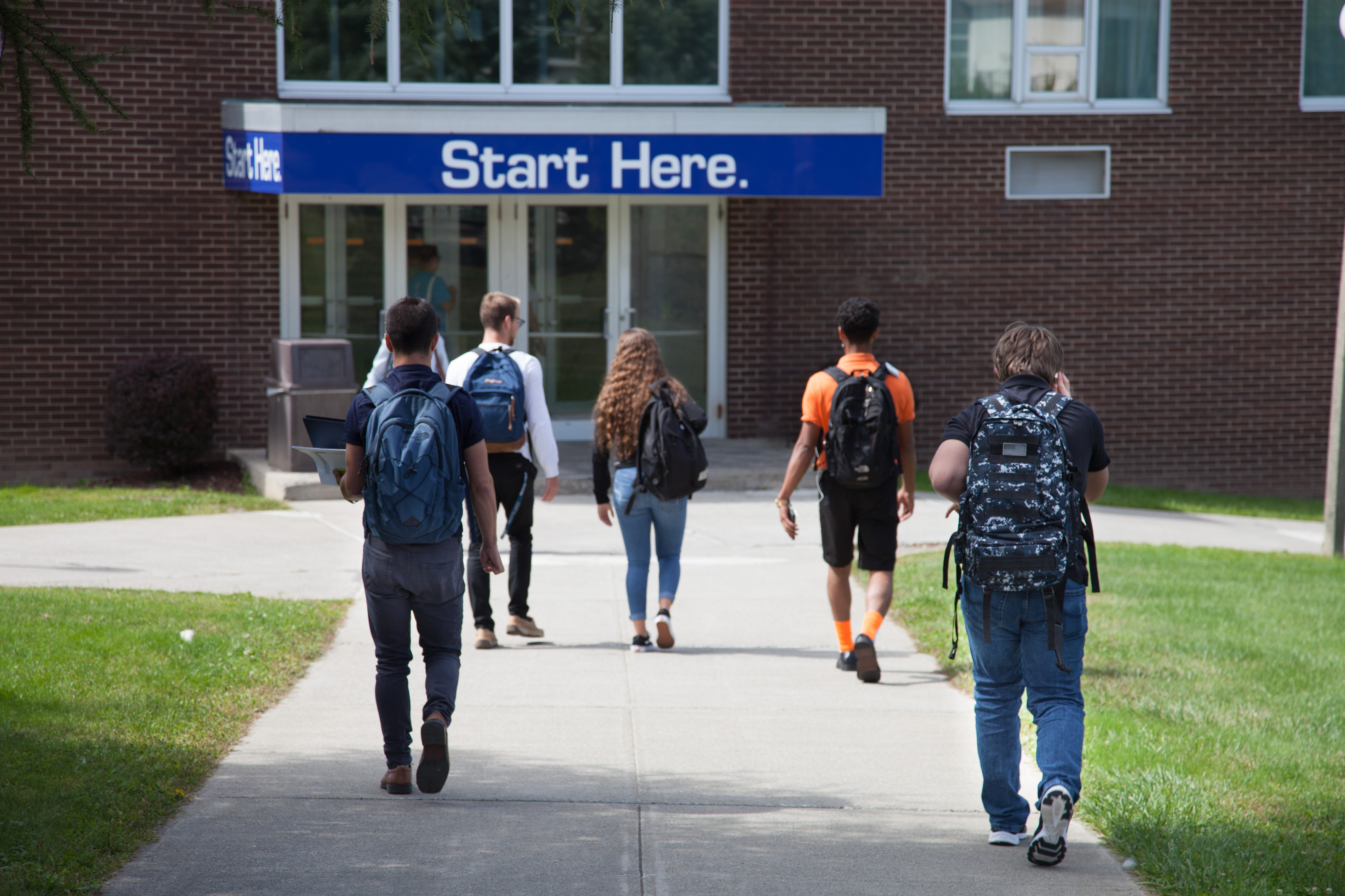 students wearing backpacks walking towards building with the words "Start Here" over entrance