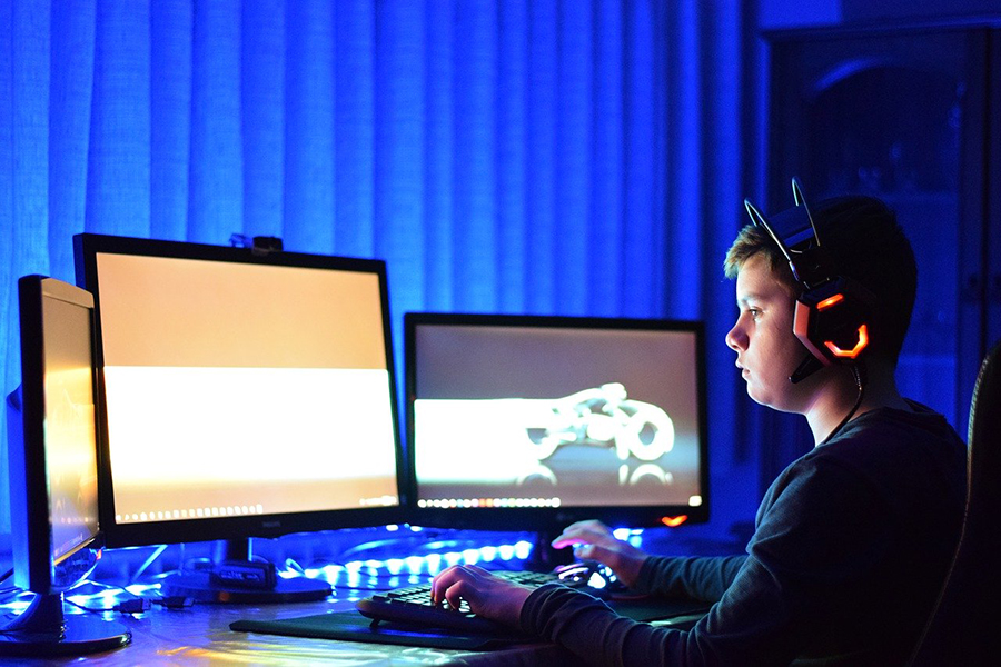 child wearing headphones with three computer screens