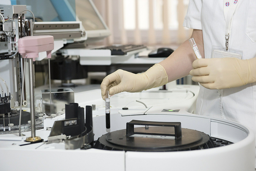 gloved hands putting tube of blood in centrifuge