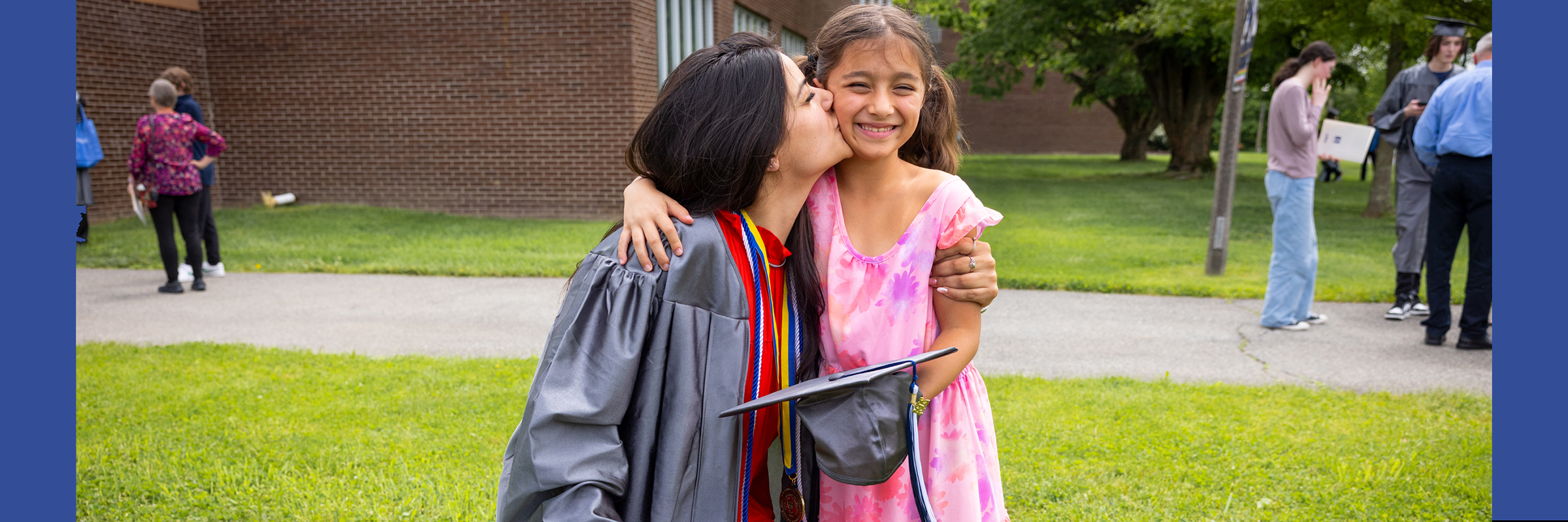 woman in graduation robe kneeling to kiss smiling young girl