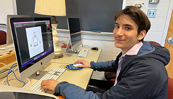 student with fcaial hair uses macintosh in classroom