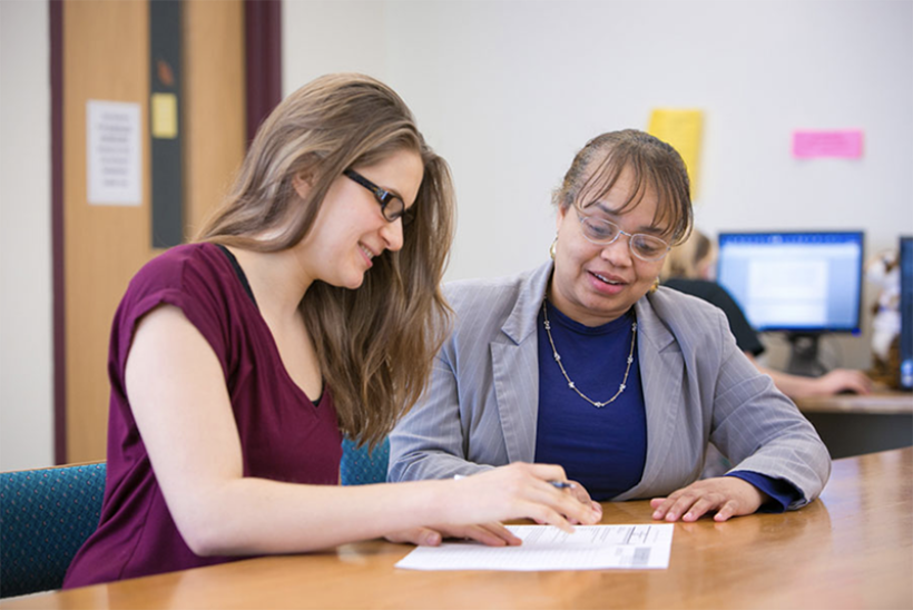 student with woman in blazer at table with papers